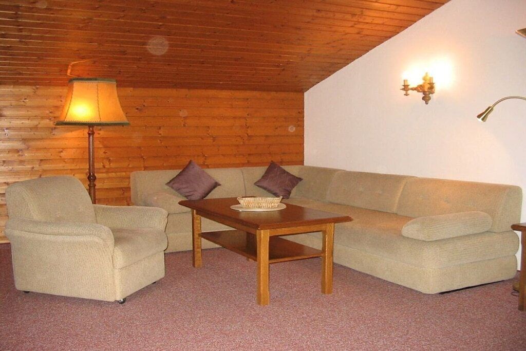 A cozy room with a wooden ceiling, a sofa, a chair, a small table, and a floor lamp.
