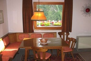 Un coin repas avec une table en bois, des bancs rembourrés de coussins rouges, une lampe suspendue et une fenêtre donnant sur un paysage verdoyant.