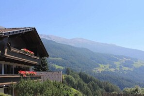 Un chalet tradicional con techo inclinado, balcones de madera con jardineras y vista a un paisaje montañoso.