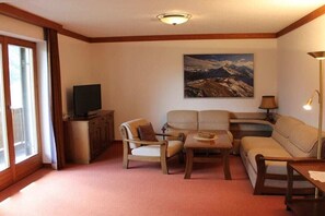 Una sala de estar acogedora con un sofá, sillones, una mesa de centro y un televisor sobre un mueble de madera.