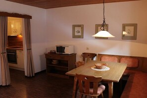 Cocina compacta con microondas, mesa de madera, sillas y una zona de comedor con banco.