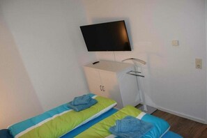 Une chambre avec un lit, un téléviseur fixé au mur, une armoire blanche et un petit bureau avec une chaise.