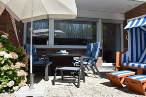 An outdoor patio with a table and chairs, a striped awning, and a brick wall. - Holiday apartment with 1 bedroom (Norden)
