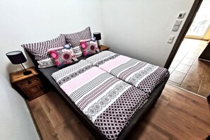 Een bed met beddengoed met een patroon, twee nachtkastjes met lampen, en een houten vloer.