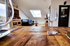 Ein Essbereich mit einem Holztisch, einem Weinglas und Blick auf ein Wohnzimmer mit einer Couch und einem Oberlicht.