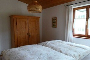 A room with a bed, a wooden wardrobe, a hanging light fixture, and a window with curtains. - Holiday apartment in Oberammergau with Wi-Fi (Oberammergau)