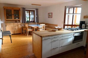 A kitchen with wooden cabinets, a dining table, chairs, and a stove. - Holiday apartment in Oberammergau with Wi-Fi (Oberammergau)