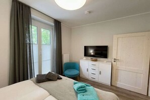A hotel room with a bed, a television, a blue chair, and a white wardrobe. - Holiday apartment with 1 bedroom (Dierhagen)