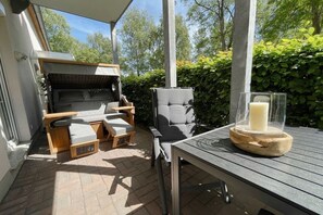 Ein Wohnmobil mit integriertem Grill und Sitzbereich, ein Tisch mit Kerze sowie Blick auf Hecke und Bäume.