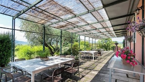 A covered outdoor dining area with tables and chairs, surrounded by greenery and a view of the landscape.