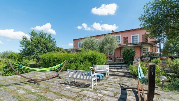 A courtyard with a hammock, a bench, and a stone pathway leading to a building with a red facade.