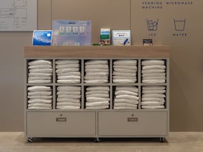 A self-service towel station with neatly folded towels, a vending machine, and signs indicating ice and water availability. - Toyoko Inn JR Uji-eki Minami-guchi (Uji)