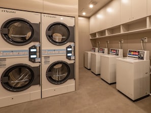 A laundry facility with multiple washing machines and dryers, including a row of white machines with digital displays and a set of black machines with a similar design. - Toyoko Inn JR Uji-eki Minami-guchi (Uji)