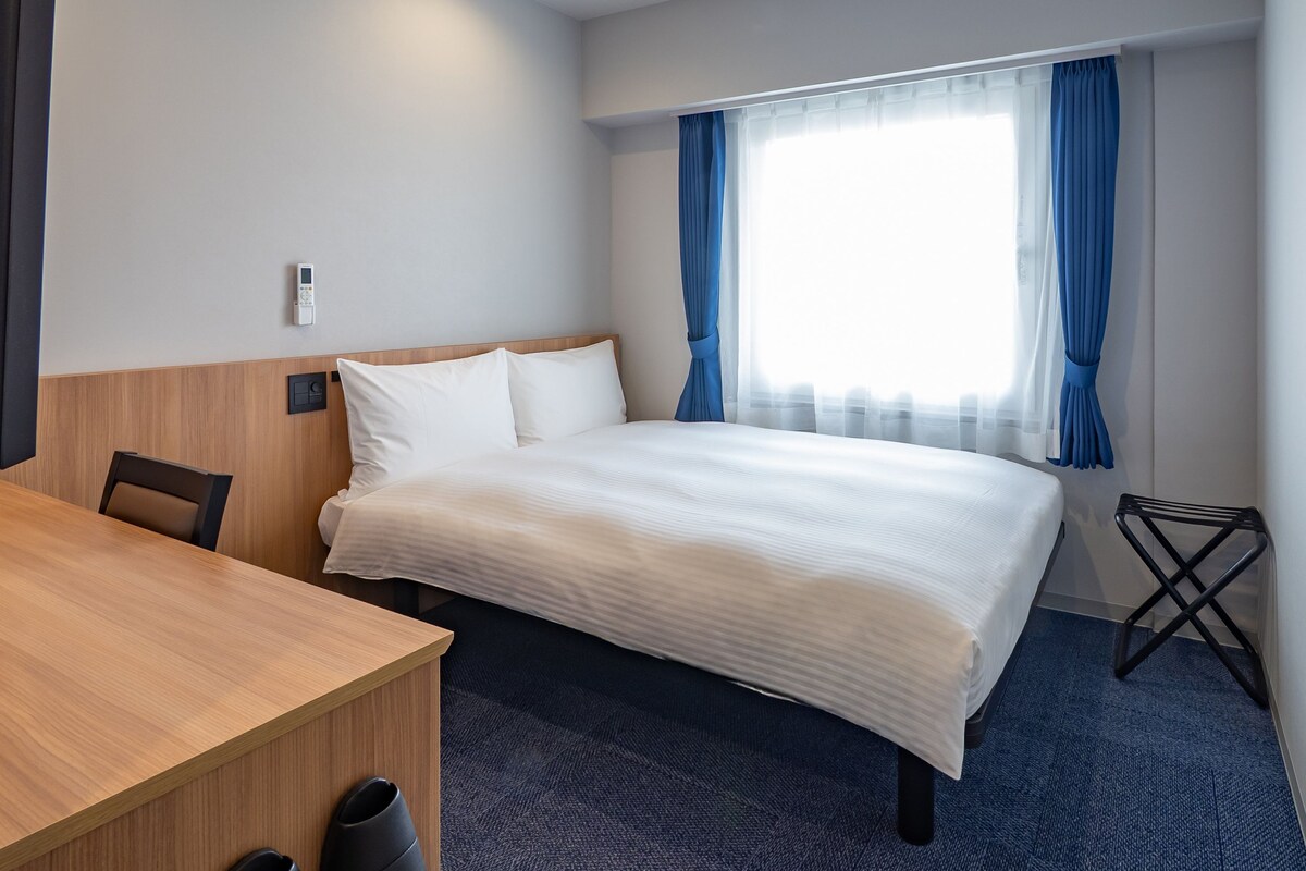 A hotel room with a bed, a desk, and a chair.