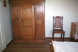 A room with a wooden wardrobe, a wooden chair, and a bed with a white bedspread. - Holiday home with 1 bedroom (Wutach- Münchingen)