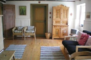 A room with a wooden floor, a wooden cabinet, a television, and two wicker chairs. - Holiday home with 1 bedroom (Wutach- Münchingen)