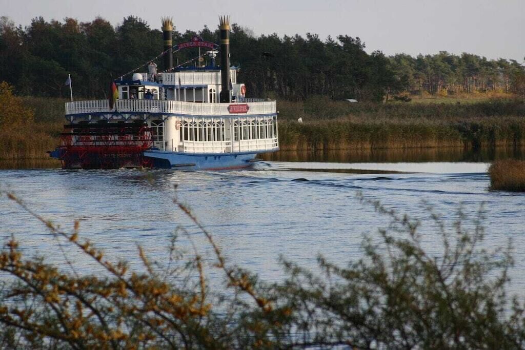 Ein Flussdampfer mit überdachter oberer Deckfläche und einer offenen unteren Deckfläche, umgeben von Wasser und Vegetation.