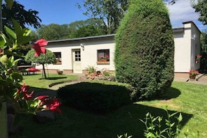 Ein weißes Gebäude mit einem gepflegten Garten, einschließlich einer ordentlich geschnittenen Hecke und Kübelpflanzen.