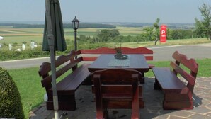 Área externa com mesas e bancos, um candeeiro e vista para o campo.