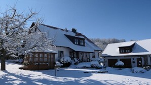 Ein verschneiter Wohnbereich mit Häusern, einer Holzhütte und einem Baum.