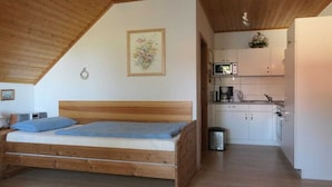 Quarto com cama de madeira e uma kitchenette no cômodo adjacente.