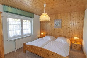 Un dormitorio con una cama de madera, dos mesitas de noche, una lámpara colgante y una ventana con persianas.