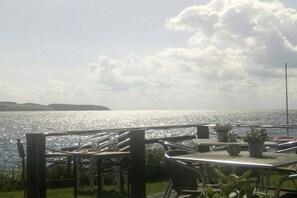 Una terraza frente al mar con vista al océano, barandas metálicas y plantas en macetas.