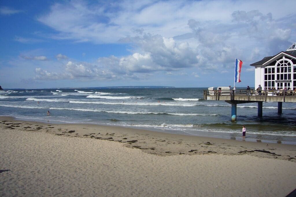 A beach with waves, a pier, and a building with a flag.