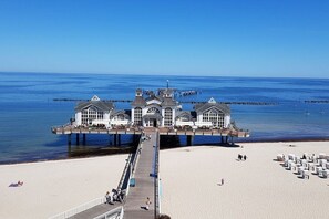 Un muelle que se adentra en el mar, con un edificio al final, una playa de arena y un cielo despejado.