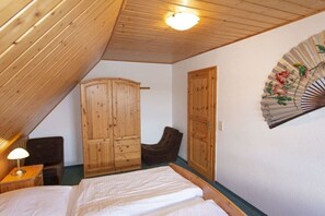 Un dormitorio con techo de madera, una cama, un armario, una silla y un ventilador de pared.