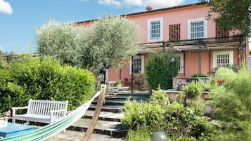 A pink building with a garden, a hammock, and a bench.