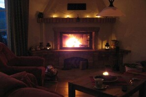 A cozy living room with a fireplace, a comfortable red armchair, and a table with a candle. - Lakeside idyll Comthurey - Reed House (Wokuhl-Dabelow OT Comthurey)