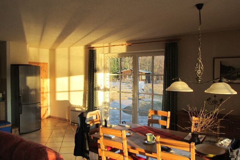 Un comedor con una mesa, sillas, un refrigerador y una ventana con vistas al exterior.