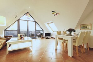 Een ruime woonkamer met hoge plafonds, een eettafel met stoelen, een bank en een televisie.