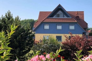 Een woonhuis met twee verdiepingen, een rood pannendak en een blauwe gevel.