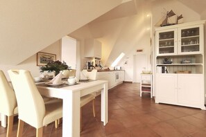 A dining area with a table and chairs, a kitchen in the background, and a cabinet with glass doors. - Holiday apartment with 2 bedrooms (Prerow)