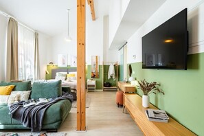 Ein modernes Wohnzimmer mit einem grünen Sofa, einem Holztisch und einem flachbildfernseher an der Wand.