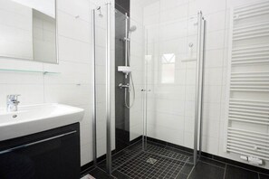 A modern bathroom with a glass-enclosed shower, a white sink, and a mirror. - Holiday apartment with 2 bedrooms (Norden)