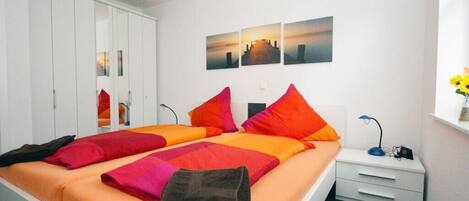 A bedroom with a bed, a nightstand, a wardrobe, and a wall with three pictures.