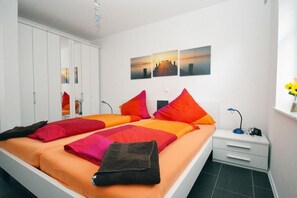 A bedroom with a bed, a nightstand, a wardrobe, and a wall with three pictures. - Holiday apartment with 2 bedrooms (Norden)