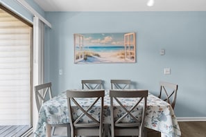 A dining area with a table set for four, a painting of an open window with a beach scene, and a light blue wall. - Glenn's Bay Retreat Surfside Beach (Surfside Beach)