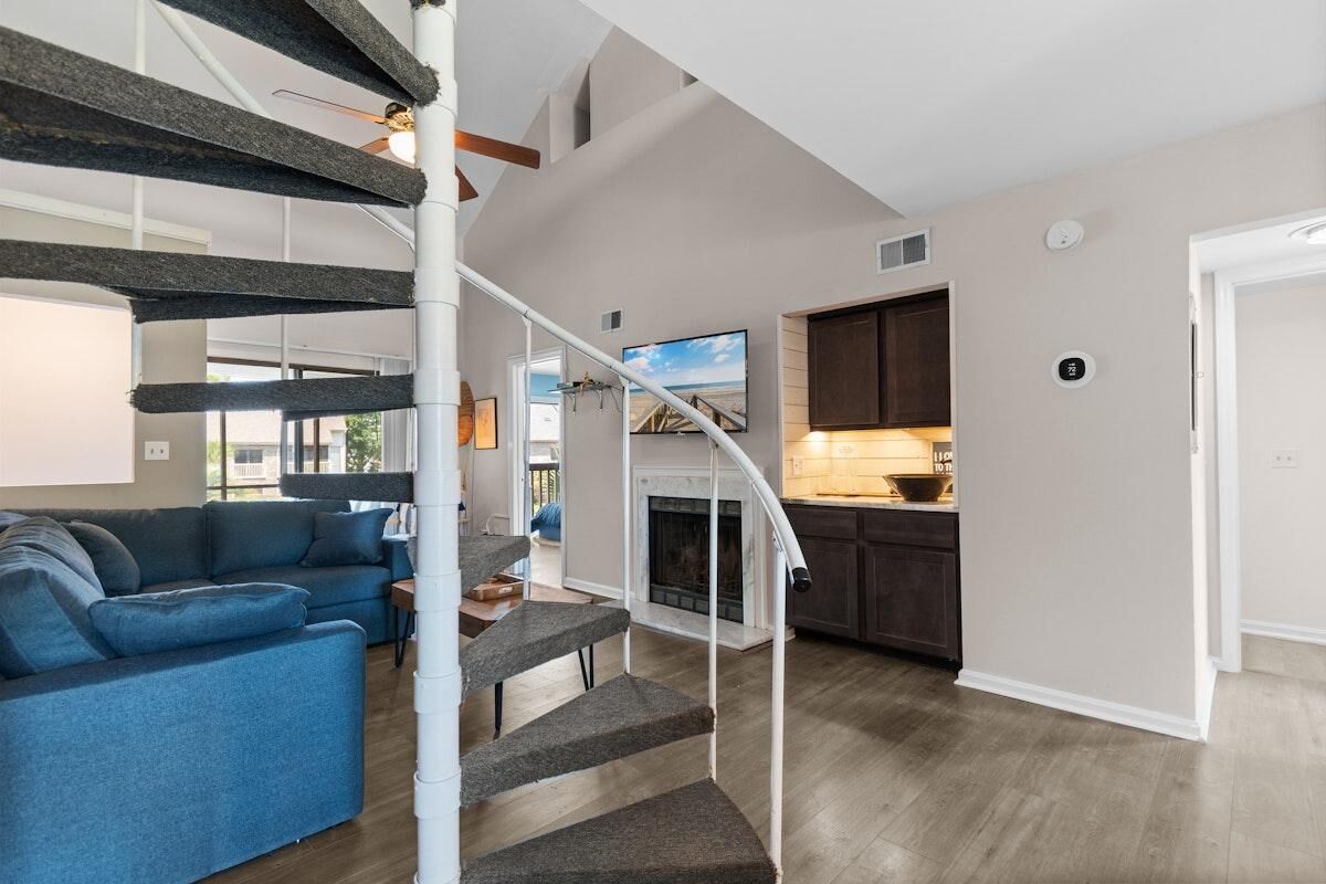 A modern interior with a staircase, a living room with a blue sofa, and a kitchen area.