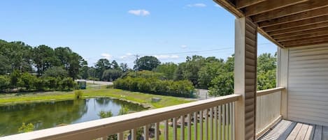 A covered balcony with a view of a pond and surrounding greenery.