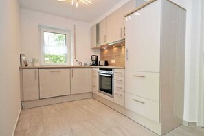 A modern kitchen with light-colored cabinets, a built-in oven, and a window with a view of greenery. - Holiday apartment with 2 bedrooms (Norden)