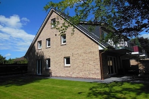 Een tweelaags gebouw van baksteen met een schuin dak, een overdekte veranda en een verzorgd gazon.