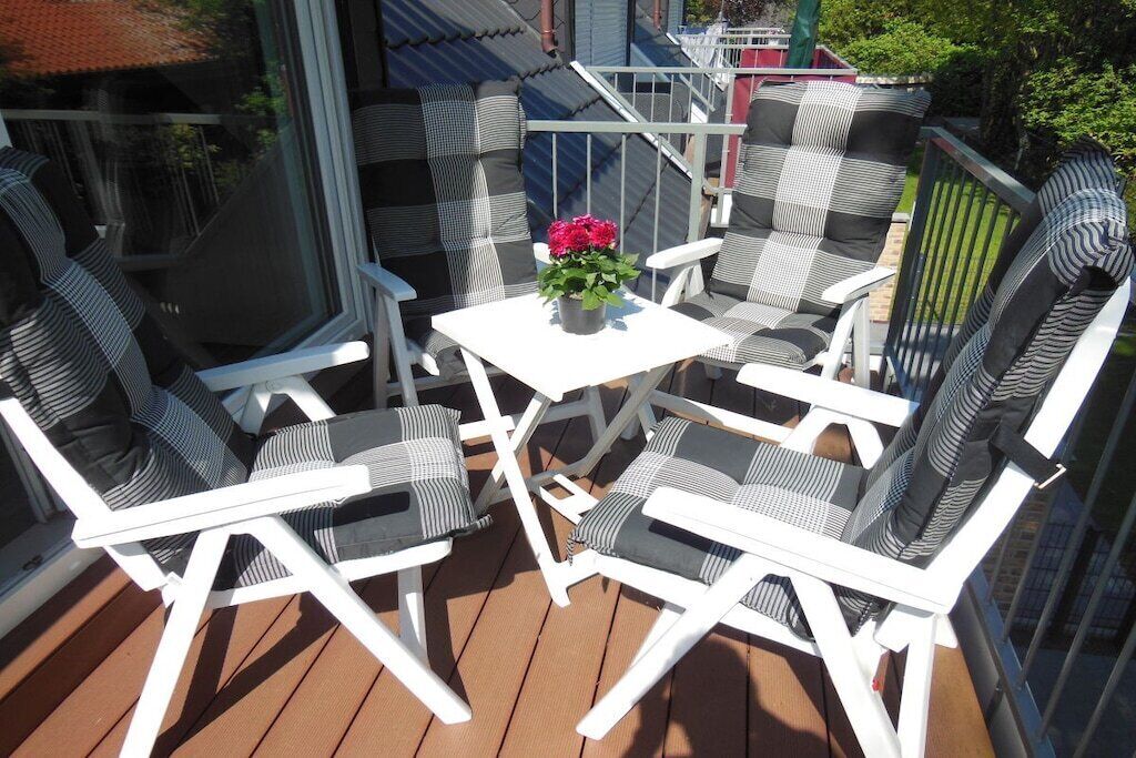 Une terrasse dotée de meubles blancs et d’une table agrémentée d’un arrangement floral.