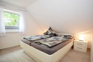 Een slaapkamer met een bed, nachtkastje, raam met gordijnen en uitzicht op groen.