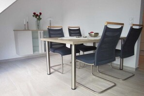 A dining area with a table and four chairs, a vase with flowers, and a small cabinet. - Holiday apartment with 2 bedrooms (Norden)