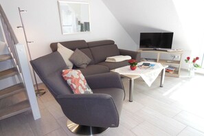 Een moderne woonkamer met een grijze bank, een klein tafeltje en een televisie.