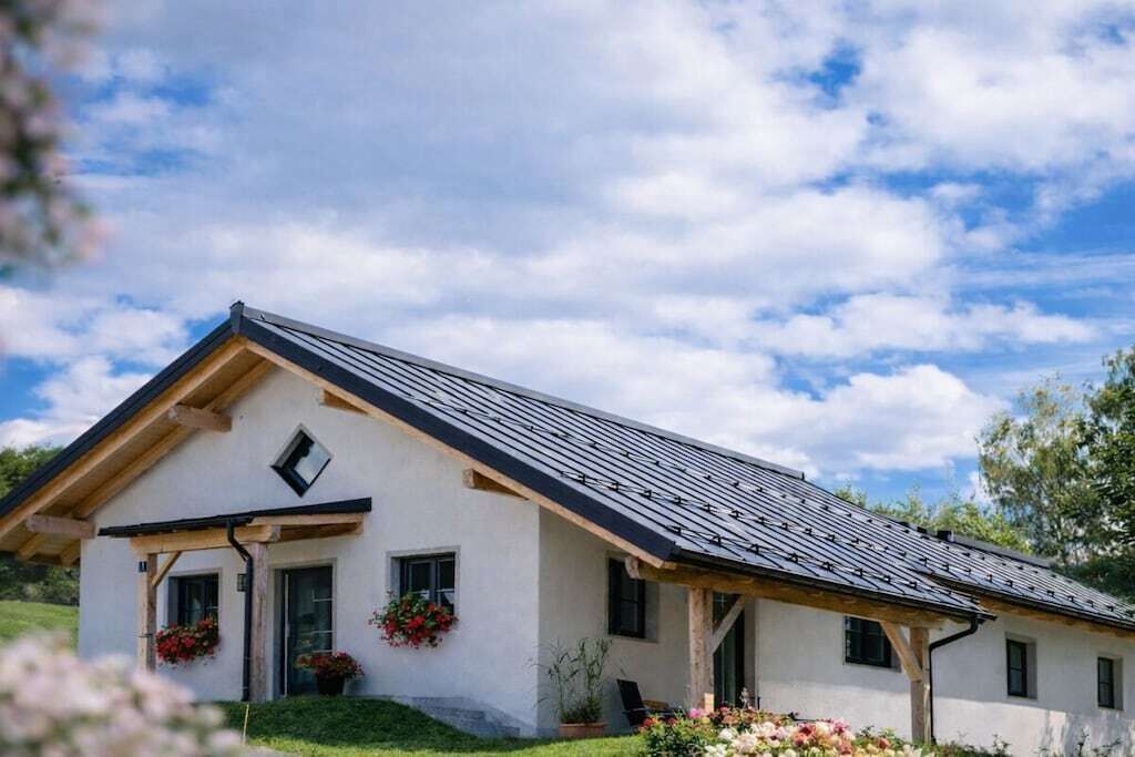Une maison de plain-pied avec un toit en pente, un porche à l’avant doté d’une balustrade en bois et une petite fenêtre.